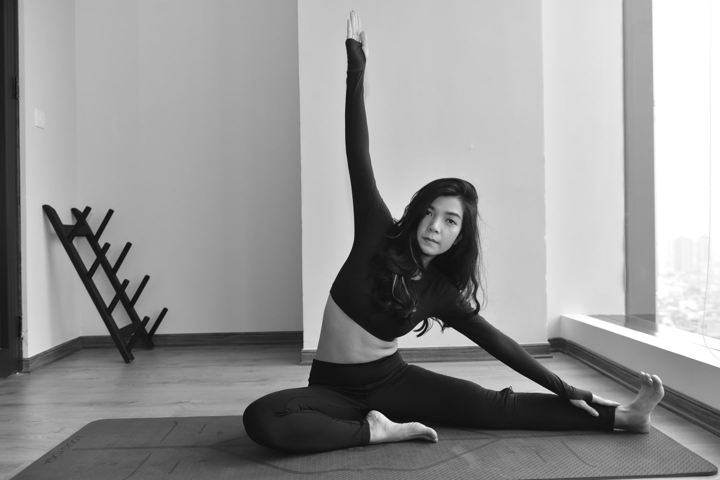 Young woman in black performing seated yoga stretch indoors, offering a calm fitness moment.